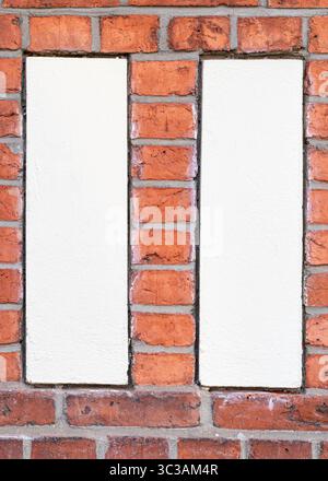 Photo symétrique face avant de deux panneaux verticaux en plâtre blanc encastrés dans un mur de briques rouges. Banque D'Images