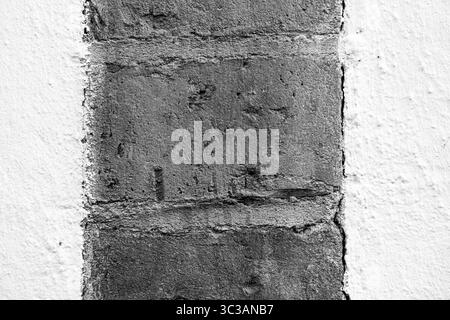 Gros plan extrême d'un segment de brique encadré par du plâtre blanc. L'image met en évidence la texture brute, les imperfections de surface. Banque D'Images