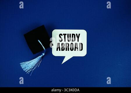 Étudier à l'étranger texte sur la bulle de discours avec la vue de dessus de chapeau de graduation sur fond bleu marine Banque D'Images
