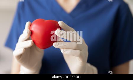 Mains du médecin cardiologue dans des gants en caoutchouc tenant le coeur rouge Banque D'Images