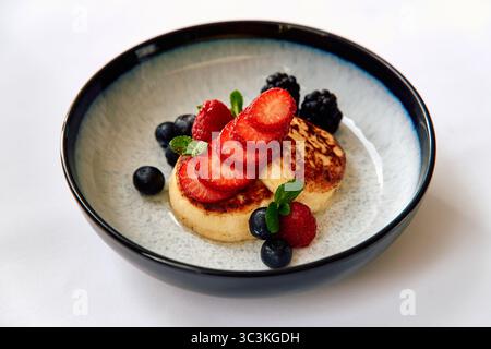 Un plat appétissant composé de crêpes moelleuses garnies de fraises fraîches, de baies mûres et d'une touche de menthe pour un délice culinaire coloré Banque D'Images
