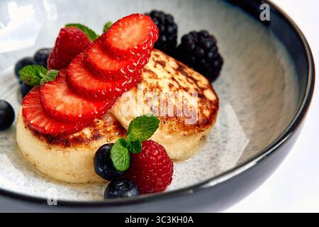 Délicieusement moelleux crêpes garnies de fraises fraîches, mûres, framboises et feuilles de menthe servies dans un bol élégant Banque D'Images