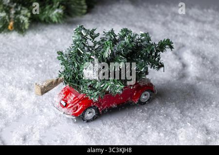 Voiture rouge jouet avec un arbre sur le toit se précipite à travers la forêt enneigée Banque D'Images