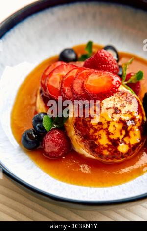 Un délicieux dessert en assiette composé de crêpes moelleuses garnies de fraises fraîches, framboises, bleuets et d'un filet de sirop sucré Banque D'Images