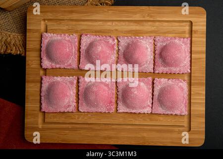 Pâtes faites à la main délicieusement élaborées : un gros plan de raviolis roses sur une planche de bois qui séduira vos papilles gustatives et inspirera la créativité culinaire Banque D'Images