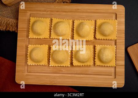 Raviolis faits maison disposés sur une planche en bois, mettant en valeur leur couleur dorée et leur forme unique, prêts à cuisiner et à déguster un délicieux repas Banque D'Images