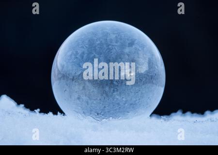 Bulle de savon gelée reposant sur la neige, motif de cristal de glace dans le froid d'hiver avec fond sombre avec espace de copie Banque D'Images