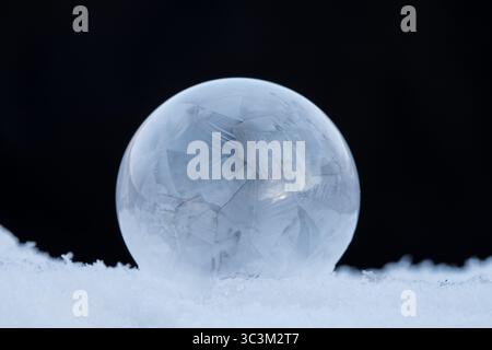Bulle de savon gelée reposant sur la neige, motif de cristal de glace dans le froid d'hiver avec fond sombre avec espace de copie Banque D'Images