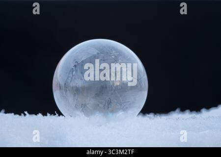 Bulle de savon gelée reposant sur la neige, motif de cristal de glace dans le froid d'hiver avec fond sombre avec espace de copie Banque D'Images