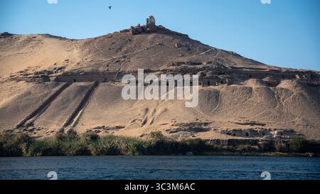 Anciennes tombes taillées dans la roche des nobles sur la colline de l'autre côté du Nil à partir d'Assouan, en Égypte, vues depuis la rive. Banque D'Images