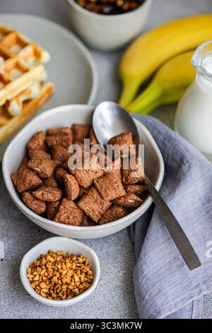 Un délicieux petit déjeuner avec un bol rempli de céréales au chocolat, accompagné de lait, gaufres, bananes et une cuillère. Le début parfait pour Banque D'Images