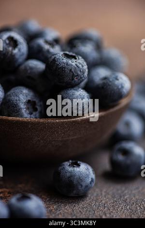 Un gros plan de bleuets frais et mûrs dans un bol en bois rustique. Les baies vibrantes sont recouvertes de rosée, soulignant leur texture juteuse et Banque D'Images