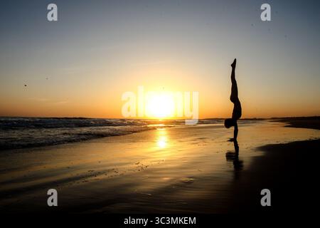 Silhouette de femme sportive dans la fabrication de la main sur la plage en face de beau coucher de soleil doré sur la mer au Portugal. Mode de vie actif Banque D'Images