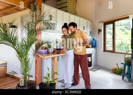 Un couple heureux profite d'un moment dans leur cuisine lumineuse, tranchant des légumes frais et préparant un repas ensemble. La salle bénéficie d'un éclairage naturel et d'une entrée Banque D'Images