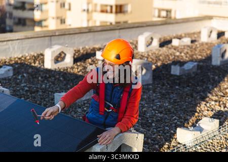 Un travailleur portant un casque de sécurité orange installe des panneaux solaires sur un toit. L'image met l'accent sur l'énergie propre et les solutions durables Banque D'Images