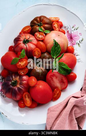 Un assortiment vibrant de tomates fraîches, y compris des variétés héritées et de cerises, magnifiquement disposées sur un plateau décoratif. Idéal pour la fabrication de refres Banque D'Images