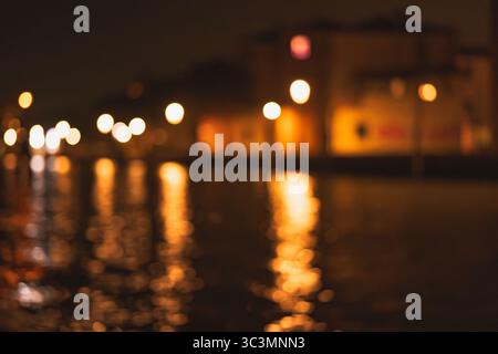 Une vue fascinante des lumières floues de la ville se reflétant spontanément sur la surface ondulante de l'eau la nuit, créant une ambiance abstraite et magique t Banque D'Images