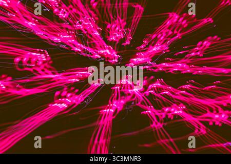 Un affichage vibrant de traînées de lumière rose capturées avec une longue exposition, créant des motifs fascinants sur un fond sombre, évoquant une sensation de mystre Banque D'Images