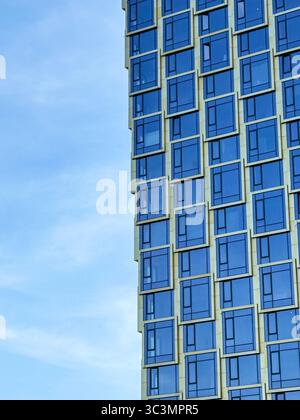 L'image montre une façade de bâtiment moderne avec de grandes fenêtres géométriques reflétant le ciel. Ce style architectural mêle urbain contemporain Banque D'Images