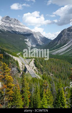 Une vue imprenable sur une route sinueuse à travers les majestueuses montagnes Rocheuses canadiennes, entourée de forêts luxuriantes et de sommets imposants sous un bleu vif Banque D'Images