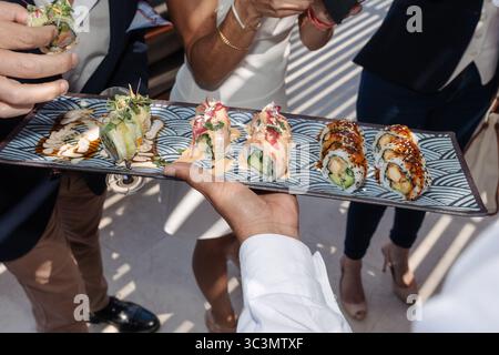 Les invités méconnus apprécient un plateau de rouleaux de sushis avec avocat, concombre et crevettes arrosés de sauces, élégamment présentés lors d'un SO Banque D'Images