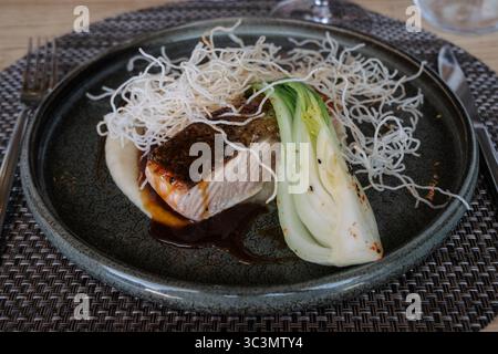 Un plat magnifiquement plaqué avec du saumon poêlé à la peau croustillante, accompagné de bok choy frais et garni de délicates nouilles croustillantes Banque D'Images