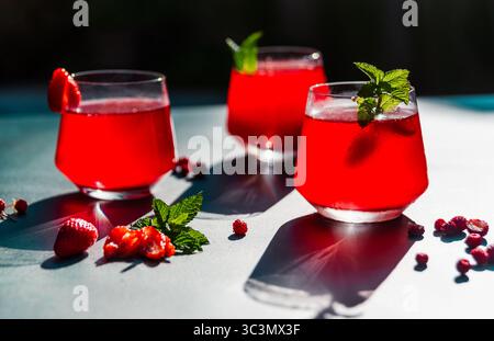 Trois verres de thé hibiscus rouge éclatant avec des fraises et de la menthe sont magnifiquement illuminés en plein soleil, créant un su rafraîchissant et frais Banque D'Images