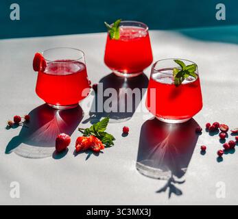 Trois verres remplis de fraises rouges éclatantes et de thé d'été froid à l'hibiscus, garnis de menthe fraîche. Parfaitement frais, capturant l'essence o Banque D'Images