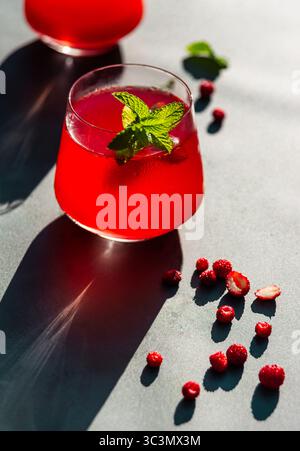 D'en haut, un thé d'été froid et vibrant avec des fraises et des hibiscus est garni de feuilles de menthe fraîche, se prélasser à la lumière directe du soleil pour un revigorati Banque D'Images