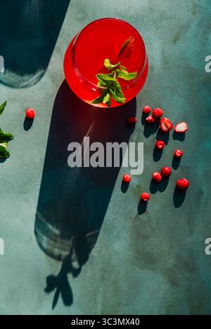 Vue de dessus d'un verre de fraises rafraîchissantes et de thé hibiscus se trouve sur une surface ensoleillée. Garnie de menthe fraîche, cette boisson rouge fraîche incarne le summ Banque D'Images