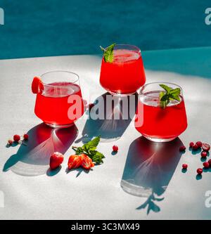 Thé froid rafraîchissant à la fraise et à l'hibiscus garni de feuilles de menthe, projetant des ombres sous la lumière du soleil. La boisson rouge éclatante invite à une fraîcheur Banque D'Images