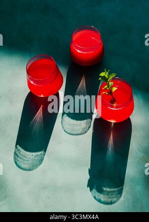 Vue de dessus du thé d'été rouge vif infusé de fraises et d'hibiscus. La boisson rafraîchissante est garnie de menthe, projetant de longues ombres en clair Banque D'Images