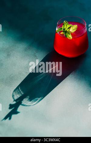 Vue de dessus de la lumière directe du soleil mettant en valeur un thé rouge vif et froid infusé de fraises et d'hibiscus, garni de menthe fraîche. Le parfait non-al Banque D'Images