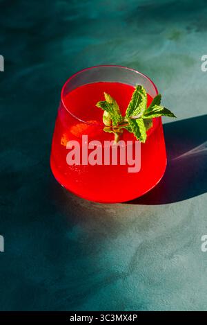 D'en haut un thé d'été froid rafraîchissant infusé de fraises et d'hibiscus, garni de feuilles de menthe fraîche. La boisson rouge éclatante est illuminée Banque D'Images