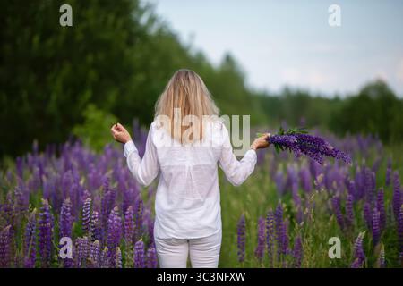 La femme admire les lupins fleuris à l'extérieur. Banque D'Images