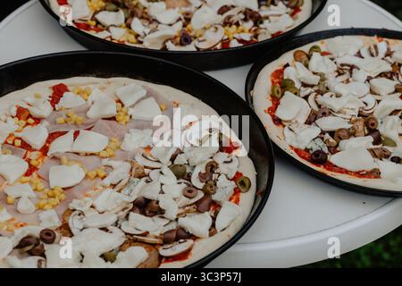 Pizza non cuite avec mozzarella, olives, champignons et sauce tomate prête pour le four Banque D'Images