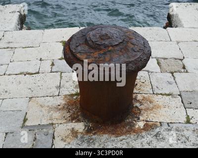 Vieux bollard d'amarrage en métal rouillé sur quai en pierre près de l'océan Banque D'Images