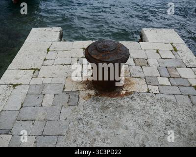 Vieux bollard d'amarrage en métal rouillé sur quai en pierre avec les vagues de l'océan hors de la jetée Banque D'Images