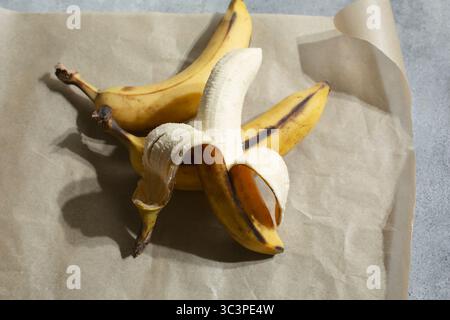 Une vue d'une banane partiellement pelée appuyée contre d'autres bananes entières. Banque D'Images