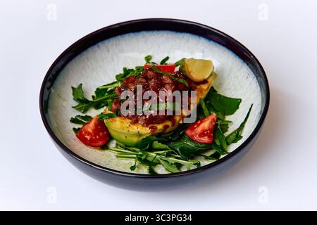 Plat vibrant avec avocat grillé garni de salsa salée, de légumes verts frais et de tomates cerises, parfaitement conçu pour les amateurs de cuisine saine Banque D'Images