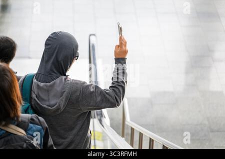 Homme portant une capuche prenant des photos en se tenant debout sur l'escalier roulant. Banque D'Images