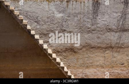 Fond avec un vieux mur sale et des escaliers qui courent le long de lui en diagonale Banque D'Images
