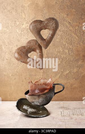 Biscuits en forme de coeur en pain d'épice volant au-dessus d'une tasse de café avec des éclaboussures Banque D'Images