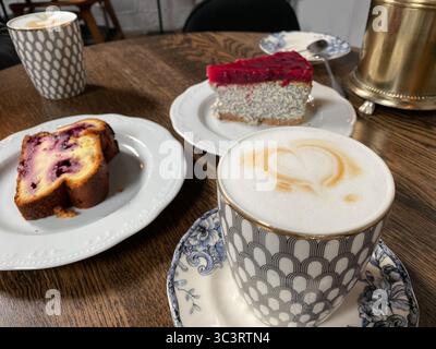 Café avec mousse de coeur et desserts sur une table en bois, avec des gâteaux dans un cadre de café confortable. Photo mobile Banque D'Images