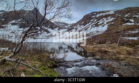 Lac gelé et rivière sauvage avec cascade des montagnes enneigées sur l'île Senja en Norvège Banque D'Images