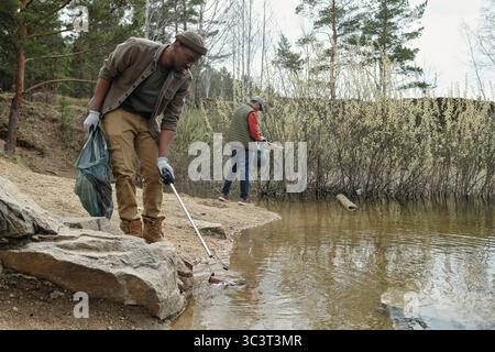 Jeune homme noir et homme caucasien d'âge moyen nettoyant Riverbank ensemble Banque D'Images