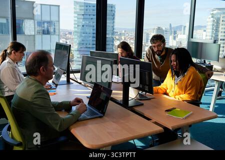 Collègues de travail travaillant sur des ordinateurs dans un bureau moderne avec vue sur la ville. Banque D'Images