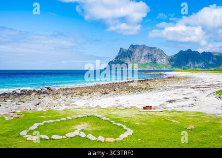 Coeur fait de pierres sur l'herbe verte et vue sur la belle plage d'Uttakleiv, côte de la mer avec des montagnes en été, îles Lofoten, Norvège Banque D'Images