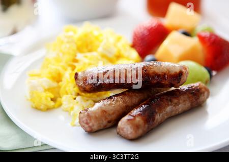 Saucisses grillées avec œufs brouillés moelleux et poivrons colorés sur assiette blanche. Copieux repas du matin protéiné plat de confort. Banque D'Images