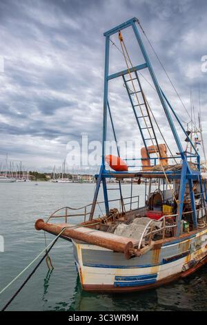 Vieux bateau de pêche traditionnel avec filets et équipement amarré à la marina de Novigrad en Istrie, Croatie. Grue de levage bleue et voiliers visibles en b Banque D'Images